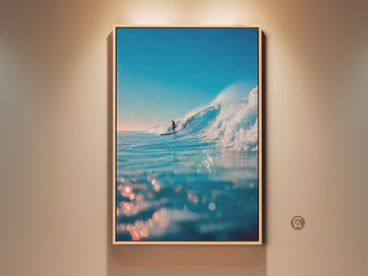 A framed ocean wave art print hangs on a wall. The artwork captures a surfer riding a large wave. The water sparkles in the sunlight. It's a beautiful piece for coastal decor. Bring the beach vibes home with this stunning ocean art.