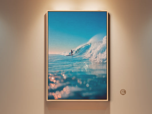 A framed ocean wave art print hangs on a wall. The artwork captures a surfer riding a large wave. The water sparkles in the sunlight. It's a beautiful piece for coastal decor. Bring the beach vibes home with this stunning ocean art.