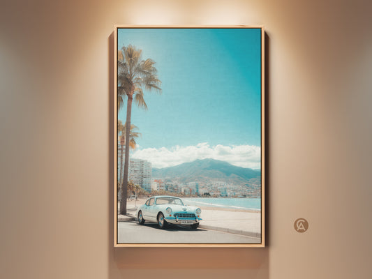 A framed artwork of a vintage white car parked on a coastal road. Palm trees line the beach with city buildings & a mountain in the background. The blue sky meets the ocean. This framed art adds a touch of retro charm to any space. Order yours today.