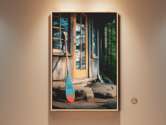 Vintage canoe paddle canvas print displayed in a neutral room. The rustic log cabin artwork is ideal farmhouse nature scene wall art. Blue and orange paddle stands by the cabin entryway. Perfect as an entryway home gift or for outdoor adventure decor.