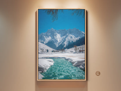 Rustic winter landscape artwork displays snow-capped mountains and a teal blue river. A scenic canvas print of nature with a clear blue sky and branches at the top of the frame. Perfect nature wall decor for outdoor enthusiasts a peaceful mountain view.