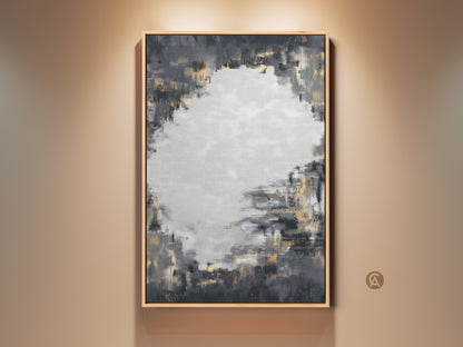 Framed charcoal grey and gold abstract artwork hangs on a neutral wall. This contemporary canvas art features textured brushstrokes. It's perfect for adding a sophisticated touch to a living room or office. The neutral color palette complements various decor styles making it a versatile piece.