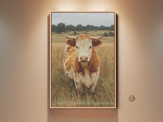 This artwork shows a close up portrait of a cow. The animal is standing in a field of tall dry grass. The color palette is mostly neutral with brown and white tones. This animal art is calming and rustic.